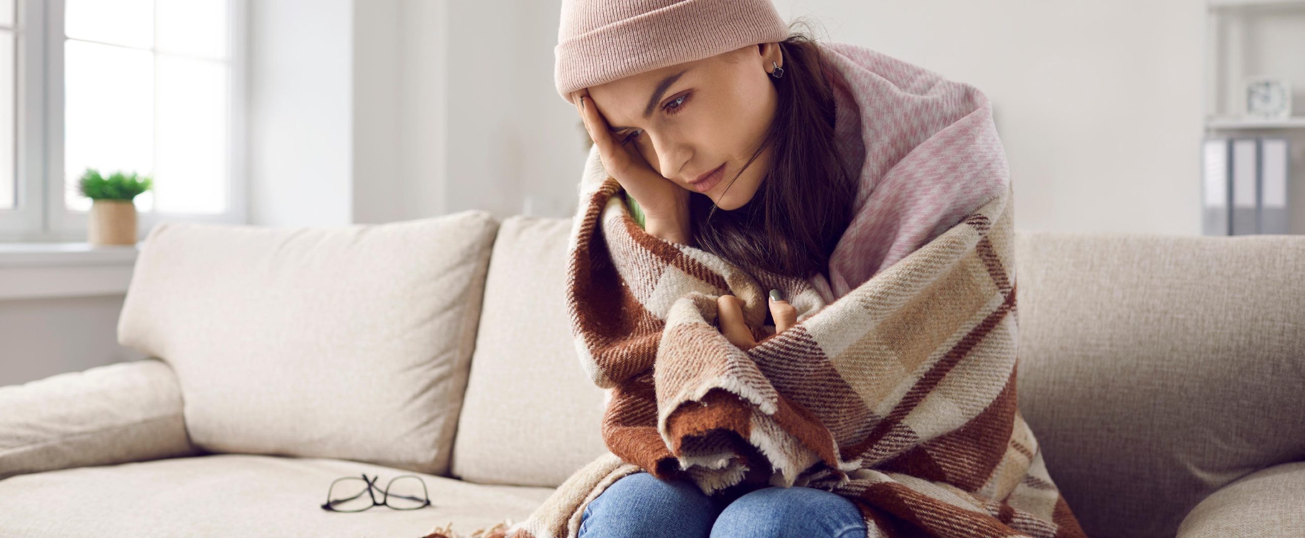 woman wearing blanket on her couch looking upset furnace not keeping up with thermostat